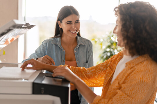 Two happy businesswomen printing documents in office