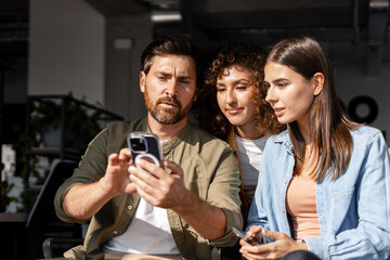Colleagues sharing engaging content on smartphone in modern office