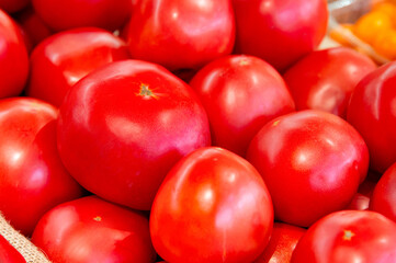 Close-up of many red large tomatoes lying in a large bin on a store counter. Tasty and healthy vegetarian food