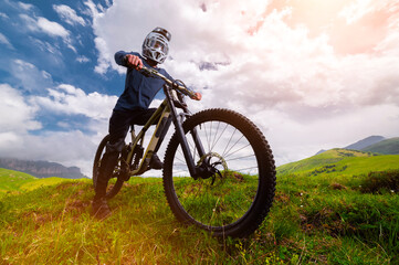 Fototapeta premium Young man standing on mountain bike or moto bike outdoors. Portrait of confident sportsman outdoors, wearing protective gear as he practices extreme sport