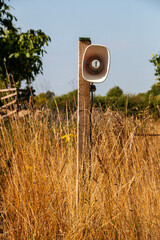 A view of a speaker on a pole in a open grass public area
