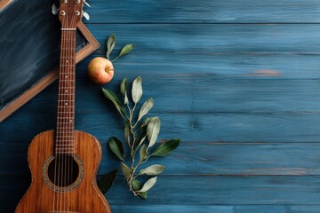 A still life features a guitar apple chalkboard and leaves on a blue wooden surface