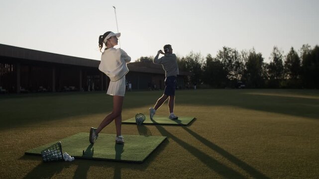 Man and woman train golf club swinging hitting balls on lawn
