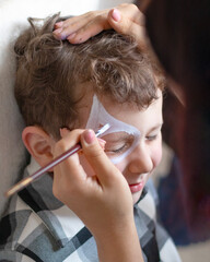 Master making aqua makeup on boys face. face painting kids. Child animator, artist's hand draw face painting. aqua grim. Fun kids activity for birthday party, holiday event or festival celebration.