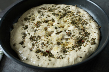 Pizza dough with spices in a black pan on a wooden table