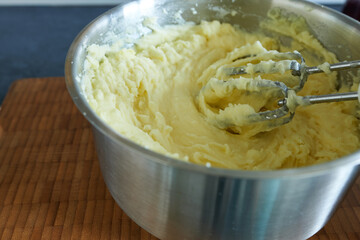 Mashed potatoes in a stainless steel bowl with a whisk on a wooden table