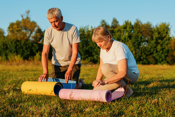 
A serious-looking senior couple is rolling up their yoga mats on a grassy field in a park after a workout.