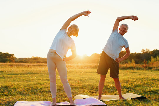 Mature couple doing a side stretch yoga pose in a grassy field during sunset.