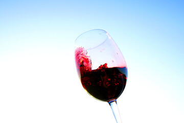 Red wine swirling on blue sky background, texture. Sommelier swirls with glass of red wine at sunset sky. Red Wine Swirling In Glass during vine Tasting or celebration vino party. Space for text