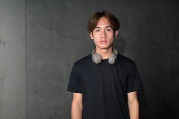 Young Thai man in black t-shirt standing near brutalist concrete wall in construction area