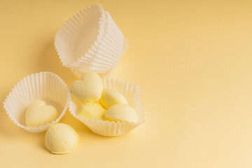 White paper tartlets with creamy yellow marshmallows in the shape of a heart on a delicate yellow background.