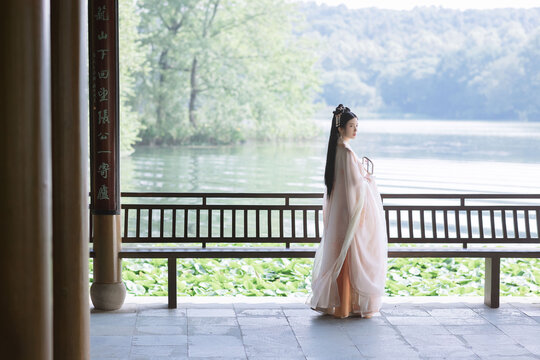 Graceful woman in a flowing pink hanfu by the serene lake.