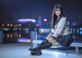 Young woman in a stylish school uniform sitting by the water at night.