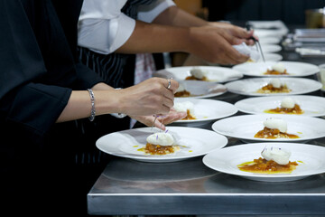 chefs in a professional kitchen garnishing dessert plates with precision. restaurant chef team showcasing fine dining presentation, culinary creativity, and teamwork in food preparation.