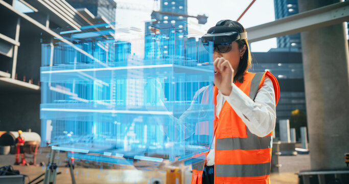 Japanese Female Architect Wearing an Augmented Reality Headset and Inspecting a Digital Hologram of a Building. Asian Civil Engineer Using a Software with Virtual Construction Plan and Interior Model