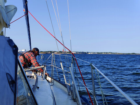 Sailman is preparing boat for docking, view from the deck of a sailing yacht towards the horizon with a distant city Hanko. Nautical adventure, travel, and connection between sea and urban landscape
