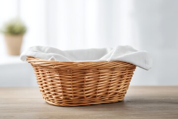 Cute wicker basket with white cloth lining, used for storage, placed on a wooden table against a blurred white background. Empty copy space for text or marketing purposes. Cotton napkin. Home decor