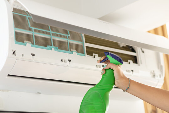 Woman cleaning a wall-mounted air conditioner filter with spray bottle