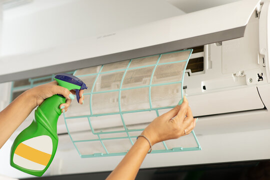 Woman cleaning a wall-mounted air conditioner filter with spray bottle