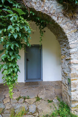 old stone wall with arch covered by green ivy and door, close up of beautiful and cozy architectural details
