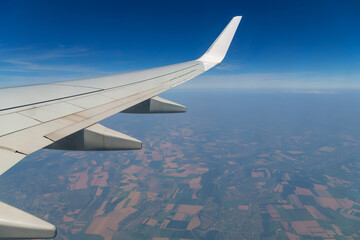 Obraz premium view from airplane window on wing and landscape below, horizon above planet and air haze, airplane view