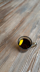 Black tea with lemon on an old wooden surface in a rustic style, top view. Pleasant wood texture, natural light create a warm, cozy atmosphere. Vertical background in natural colors with  text space 