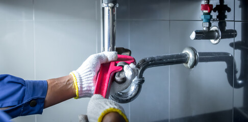 Plumber hands holding wrench doing repairing work at the sink and clogged pipe in bathroom carefully