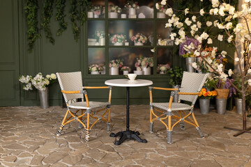 Empty interior outdoor cafe terrace with table and chair. Green exterior of the outside restaurant with furniture. Cozy street French-style cafe. Facade of coffee house and flower shop with bouquets	
