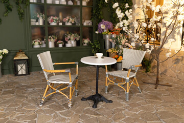 Empty interior outdoor cafe terrace with table and chair. Green exterior of the outside restaurant with furniture. Cozy street French-style cafe. Facade of coffee house and flower shop with bouquets	

