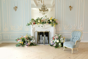 Classic elegant festive living room interior historic design chic furniture, decorated white fireplace with flowers and plants, candles, chandelier and blue armchair carved legs in the Baroque	
