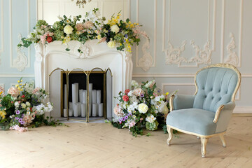 Classic elegant festive living room interior historic design chic furniture, decorated white fireplace with flowers and plants, candles, chandelier and blue armchair carved legs in the Baroque	
