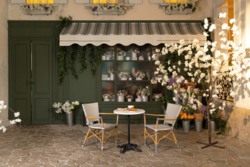 Empty interior outdoor cafe terrace with table and chair. Green exterior of the outside restaurant with furniture. Cozy street French-style cafe. Facade of coffee house and flower shop with bouquets	
