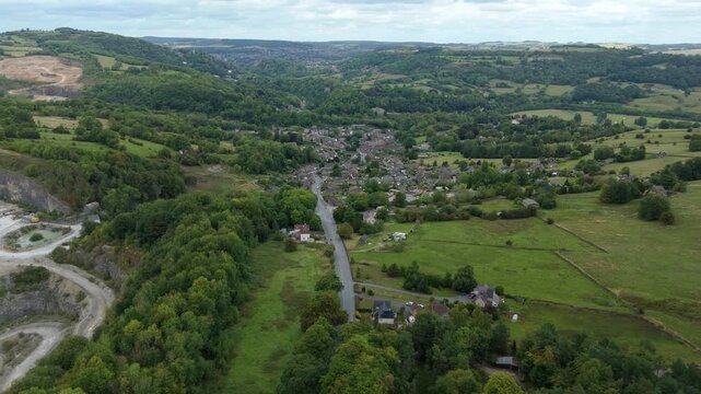 Aerial panning drone footage of Derbyshire heritage village with stone homes and scenic green valley surrounded by rural hills England UK