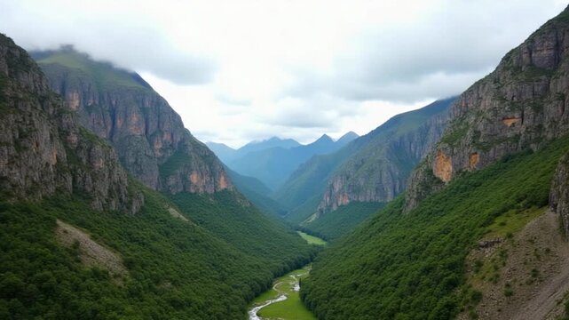 A serene mountain valley in Kyrgyzstan, captured with a static handheld phone camera. Rocky cliffs, lush greenery, and distant peaks create a rugged natural scene under a cloudy sky.