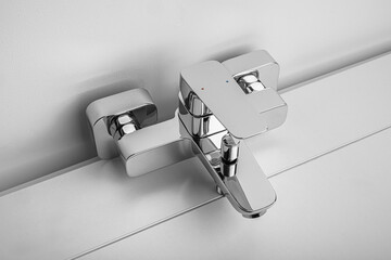 A sleek modern chrome faucet is shown installed against a white bathroom wall.