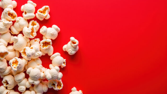 Crispy popcorn scattered on vibrant red background creates playful and inviting atmosphere, perfect for movie nights or snacks