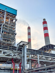 Fototapeta premium Industrial Power Plant Exterior Under a Pale Sky Featuring Tall Chimneys and Complex Pipe Systems for Energy Production and Global Warming Prevention