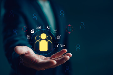 Businessman holding virtual CRM icon with people, data charts and target analytics. Concept of customer relationship management, marketing strategy, sales growth and client engagement.