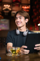 Young Thai Asian man using digital tablet computer and drinking tea