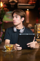 Young Thai Asian man using digital tablet computer and drinking tea