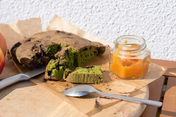 Gluten free homemade spinach cake with plums, served with homemade apricot jam, knife and spoon on wooden board