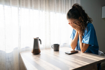 Sad nurse sitting at table covering face with hands
