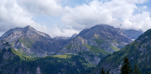 Fototapeta premium Majestic mountain landscape showcasing rugged peaks and lush green valleys under a bright blue sky with fluffy clouds, representing the beauty of nature and outdoor adventure