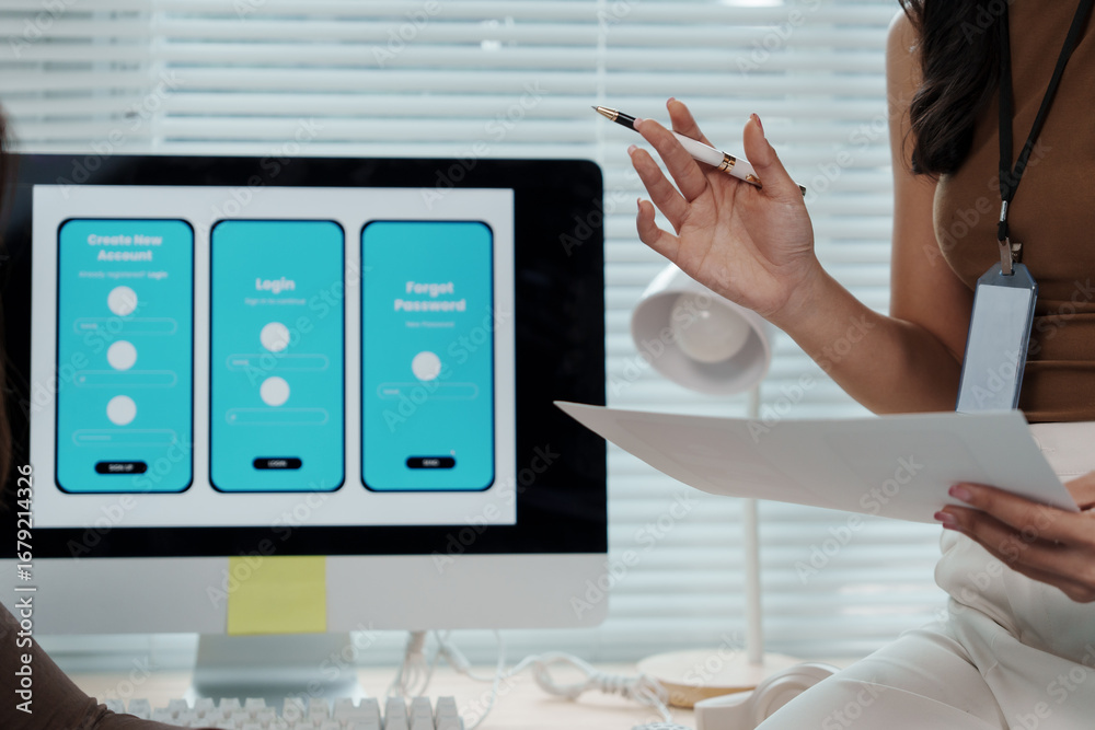 Wall mural web designer holding documents while pointing at a computer screen displaying a mobile app design, c