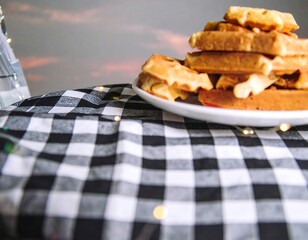 Stacked waffles on a checkered tablecloth at sunset
