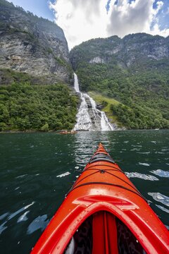 Kayak trip on the Geirangerfjord at the Freier waterfall, tip of a red kayak in the fjord, atmospheric fjord landscape, first person view, near Geiranger, M&oslash;re og Romsdal, Norway
