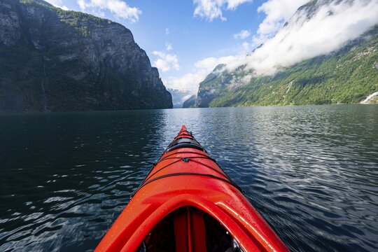 Kayak trip on the Geirangerfjord, tip of a red kayak in the fjord with reflection, atmospheric fjord landscape, first person view at Geiranger, M&oslash;re og Romsdal, Norway