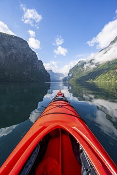 Kayak trip on the Geirangerfjord, tip of a red kayak in the fjord with reflection, atmospheric fjord landscape, first person view at Geiranger, M&oslash;re og Romsdal, Norway