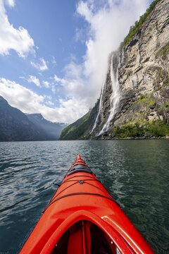 Kayak trip on the Geirangerfjord at the waterfall The Seven Sisters, tip of a red kayak in the fjord, atmospheric fjord landscape, first person view, near Geiranger, M&oslash;re og Romsdal, Norway