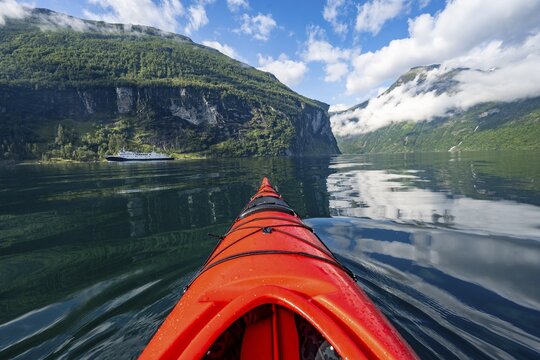 Kayak trip on the Geirangerfjord, tip of a red kayak in the fjord with reflection, atmospheric fjord landscape, first person view at Geiranger, M&oslash;re og Romsdal, Norway